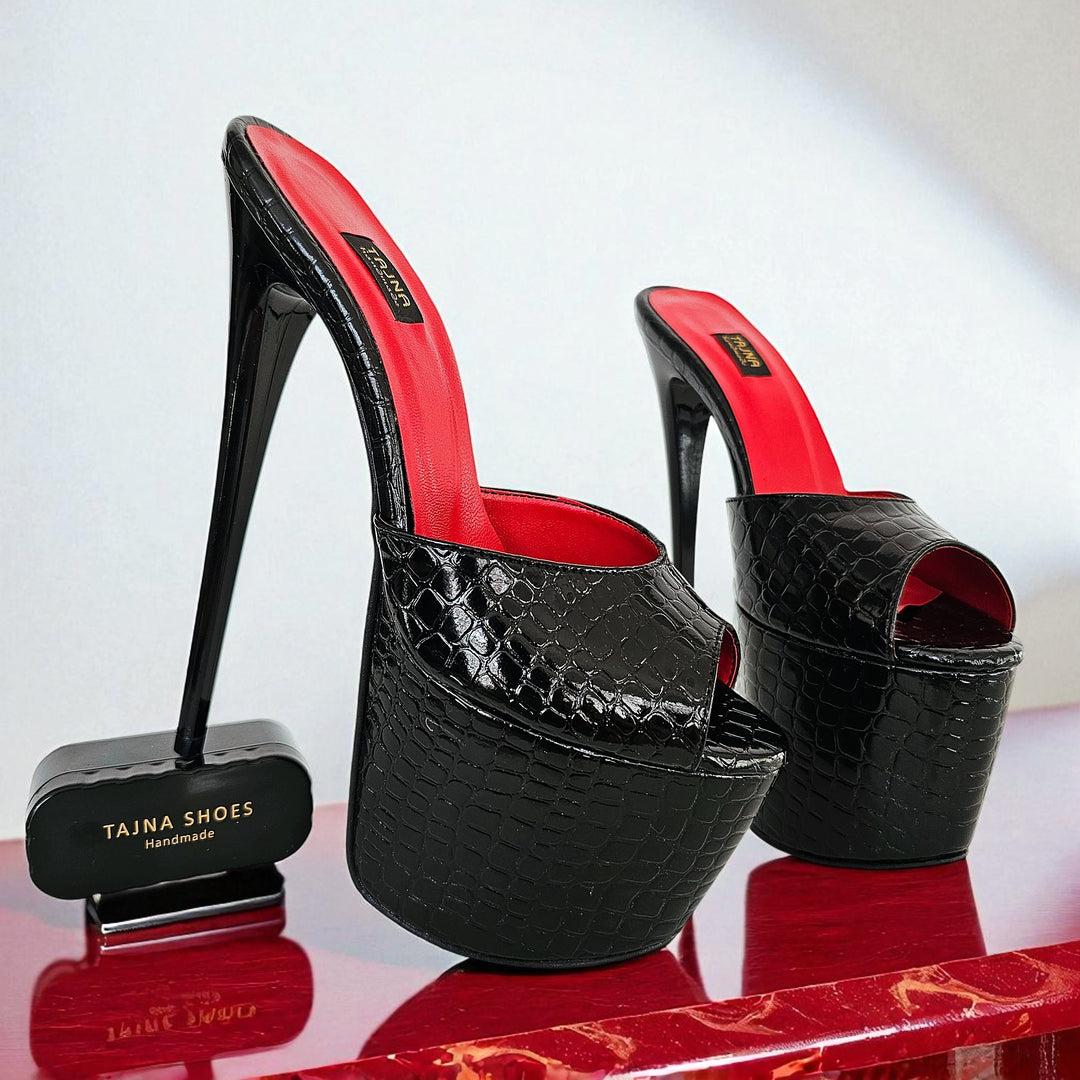 Black high-heeled shoes with red interior on a reflective surface, branded 'Tajna Shoes'.