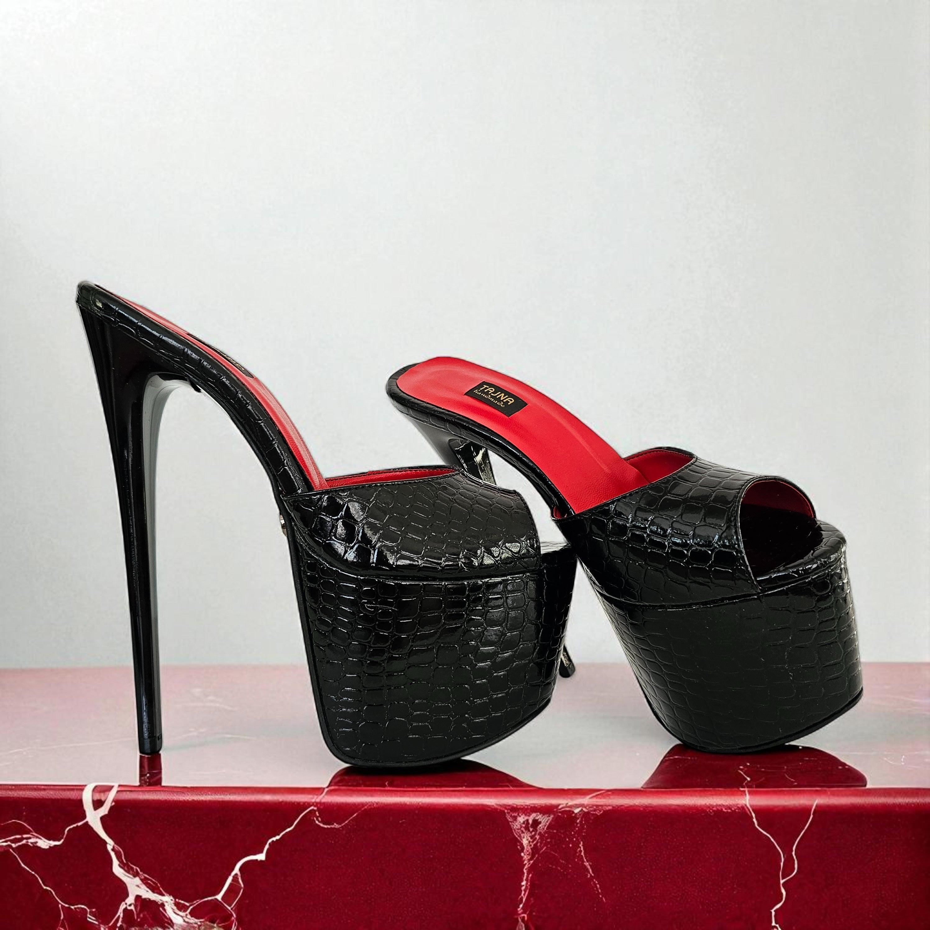 Black high-heeled shoes with red interior on a red marble surface