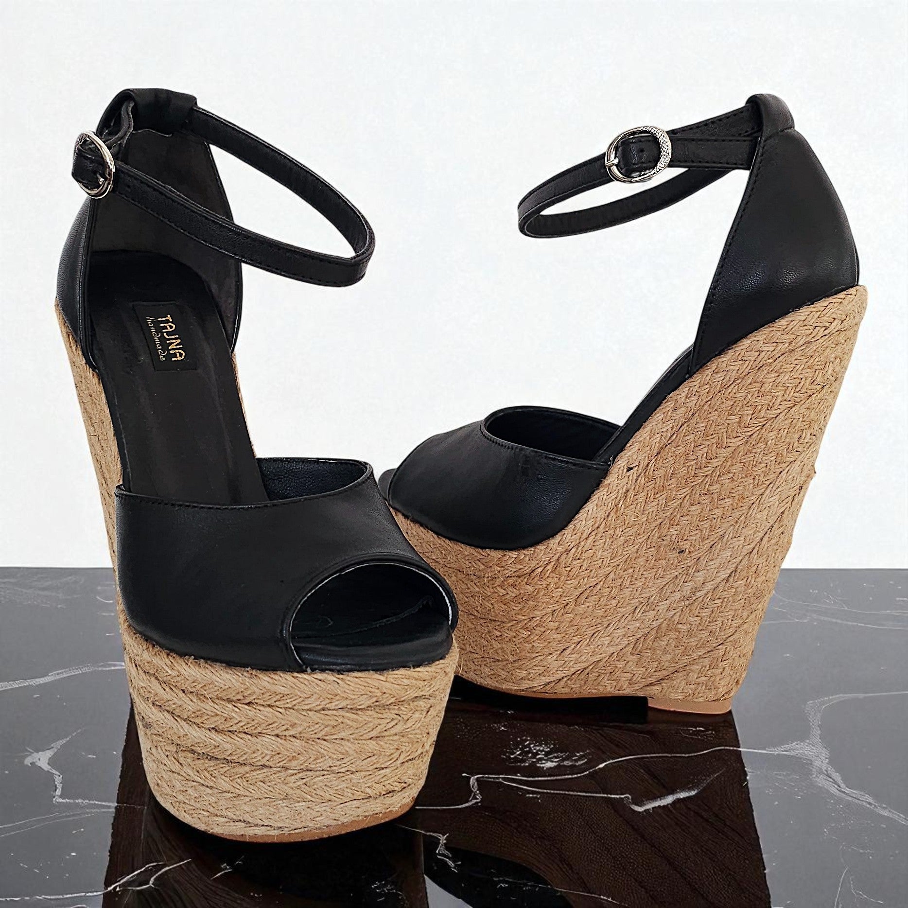 Black wedge sandals with jute sole on a reflective surface