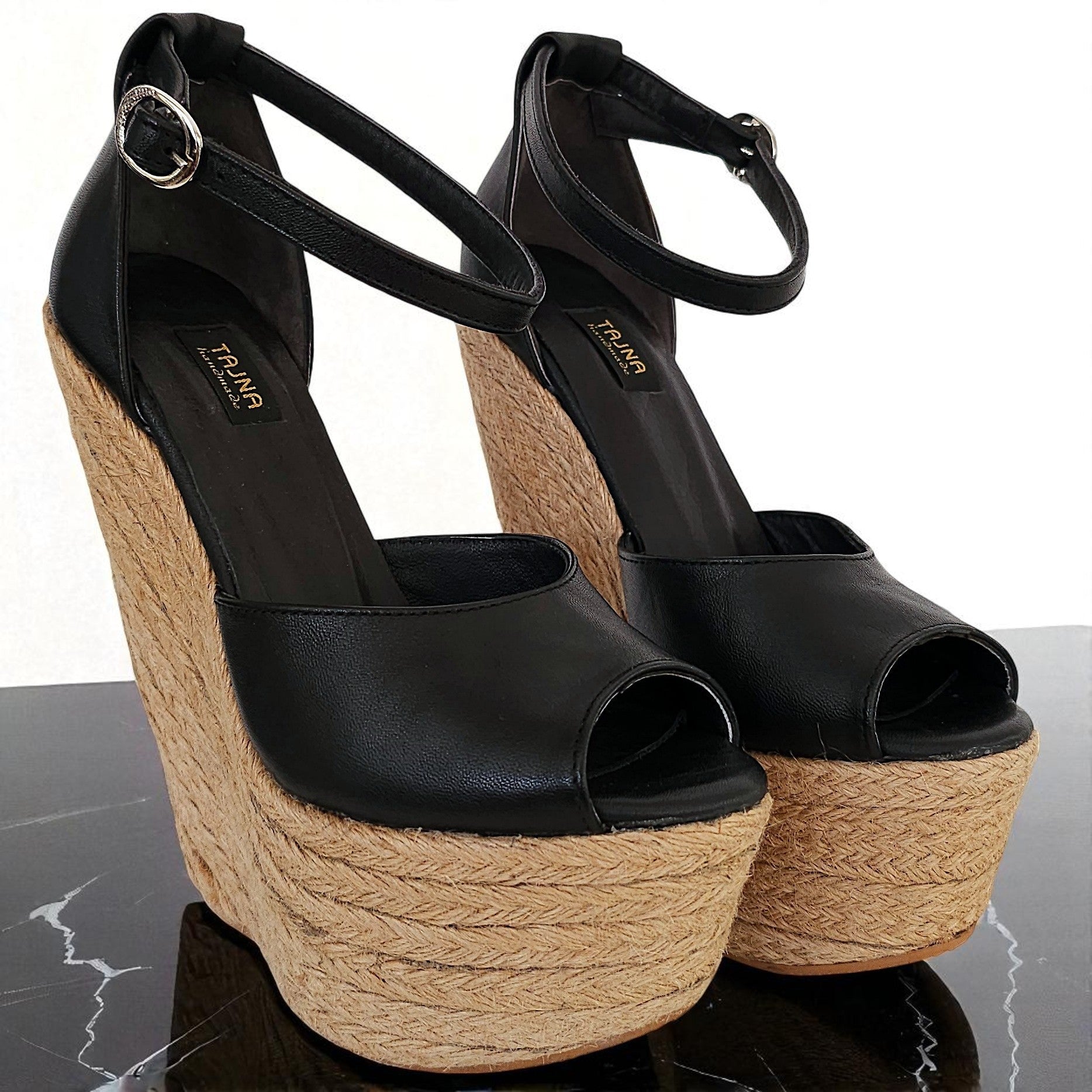 Black wedge sandals with jute sole on a reflective surface
