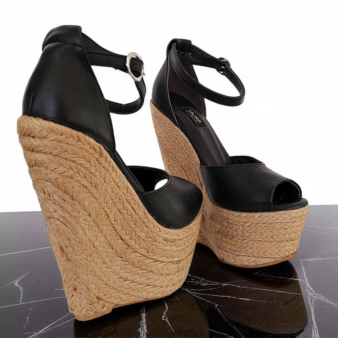 Black wedge sandals with jute sole on a reflective surface