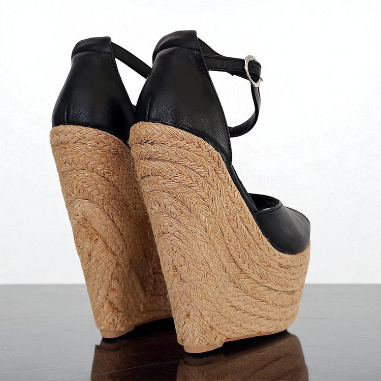 Black wedge sandals with woven brown soles on a reflective surface.