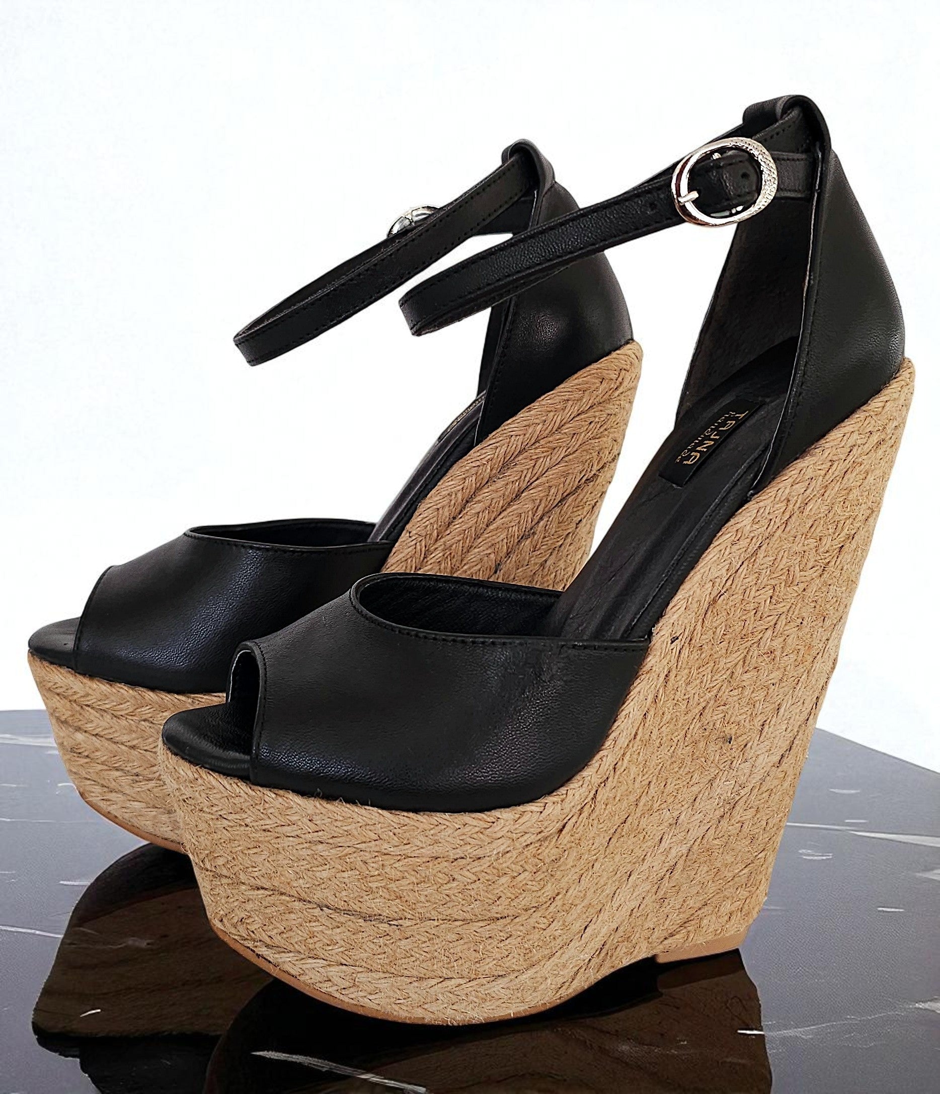Black wedge sandals with cork platforms on a reflective surface