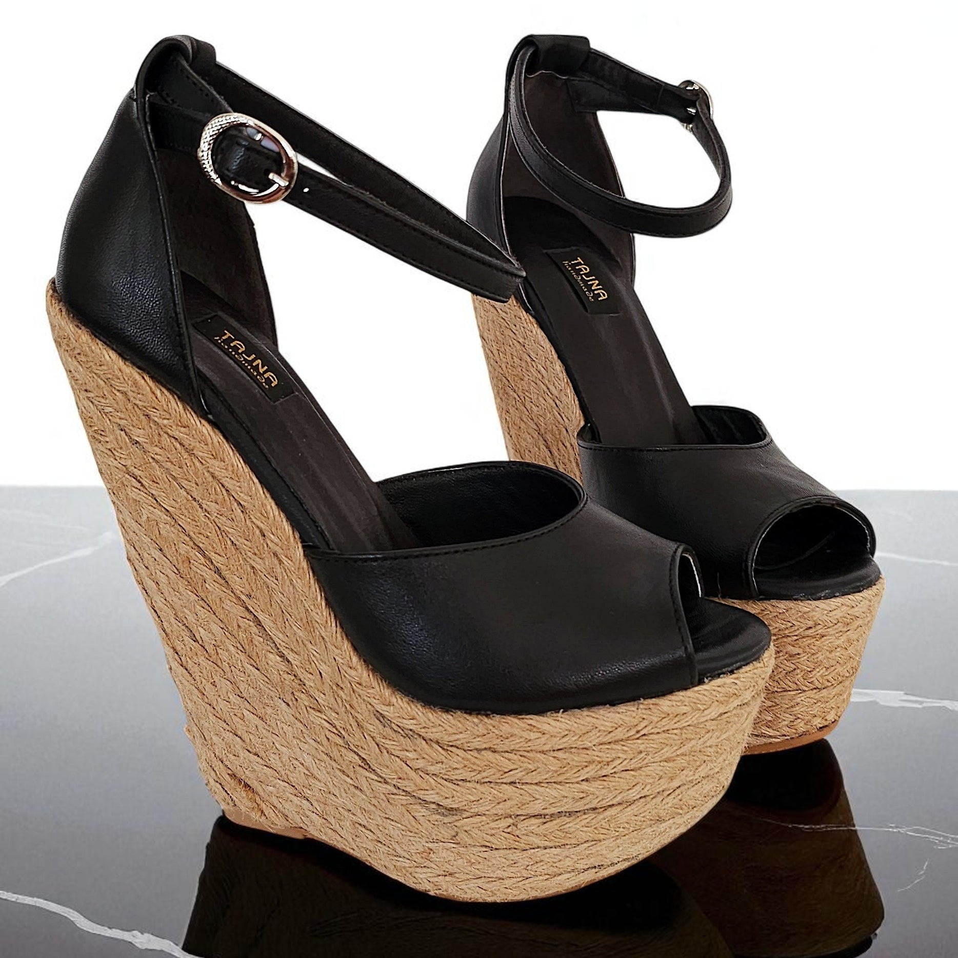 Black wedge sandals with jute sole on a reflective surface