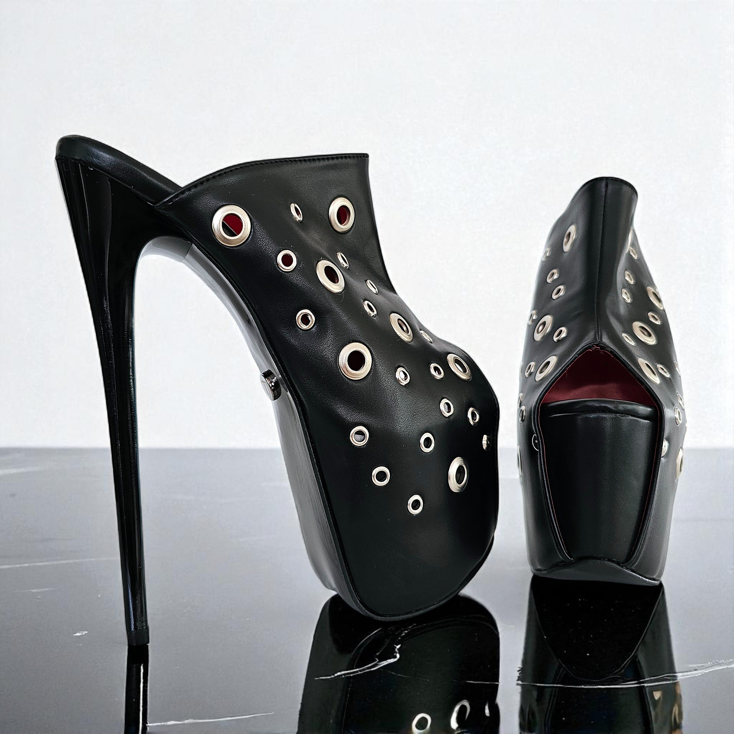 Black high-heeled shoes with eyelet design on a reflective surface