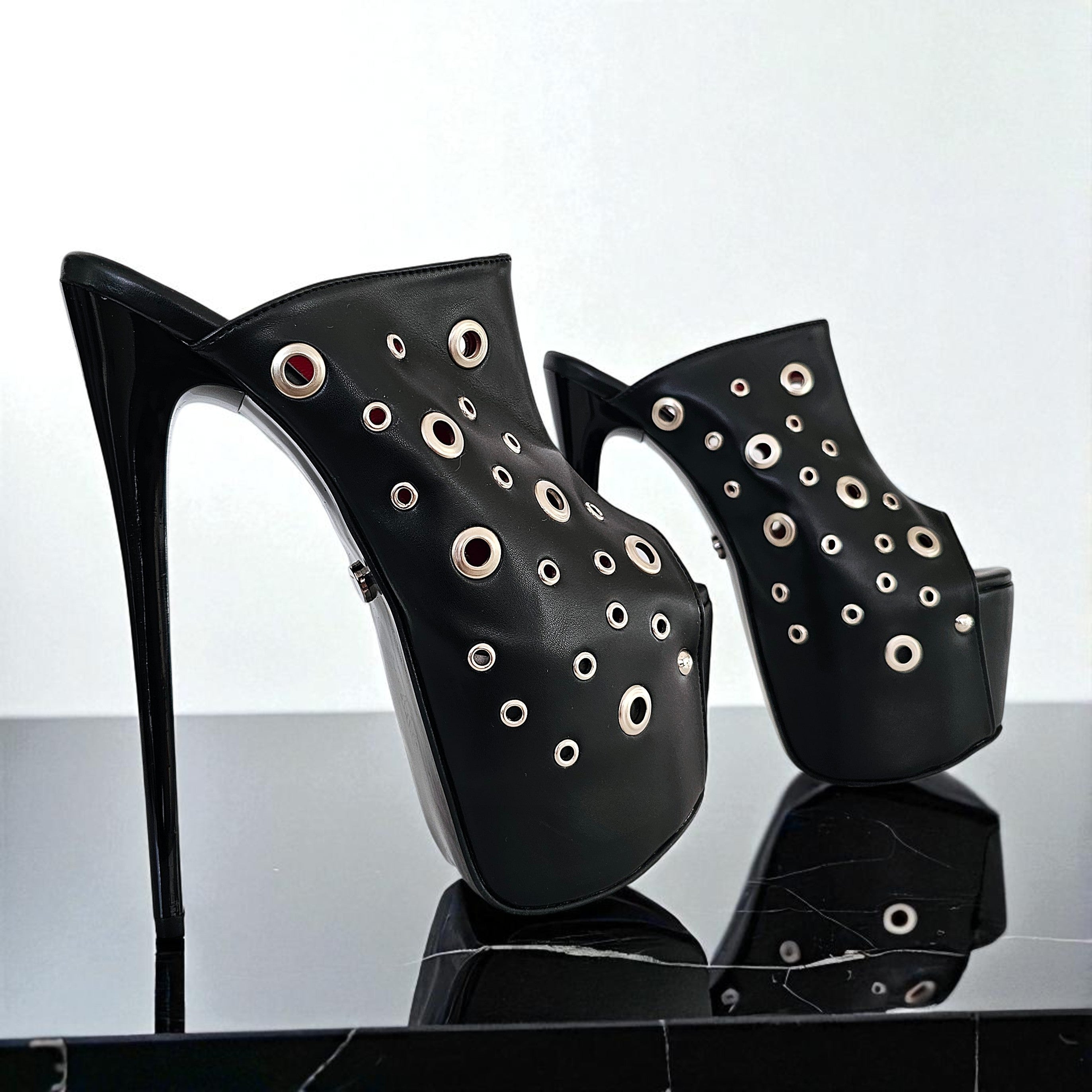 Black high-heeled shoes with eyelet details on a reflective surface.