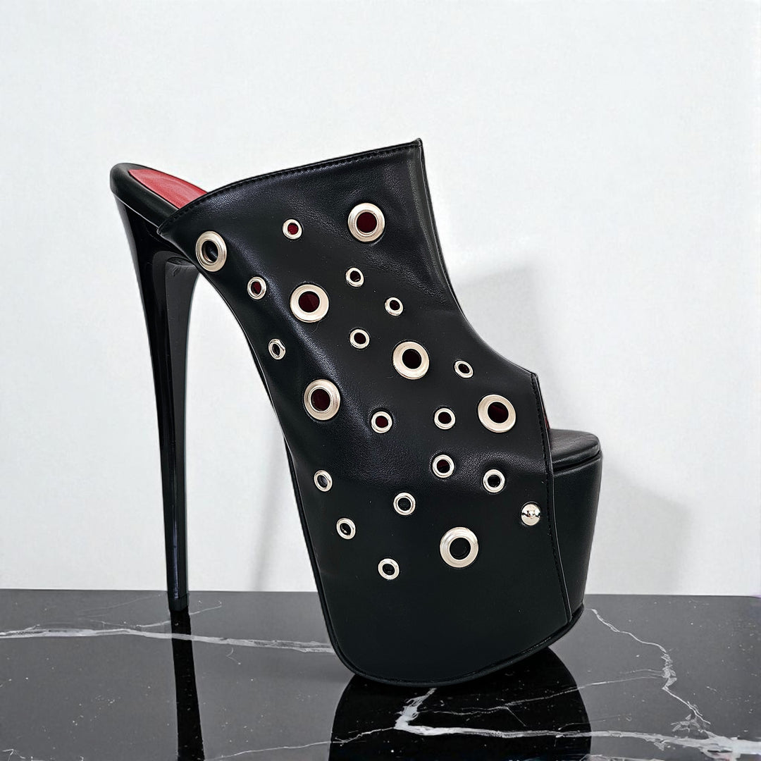 Black high-heeled shoe with circular cutouts on a marble surface