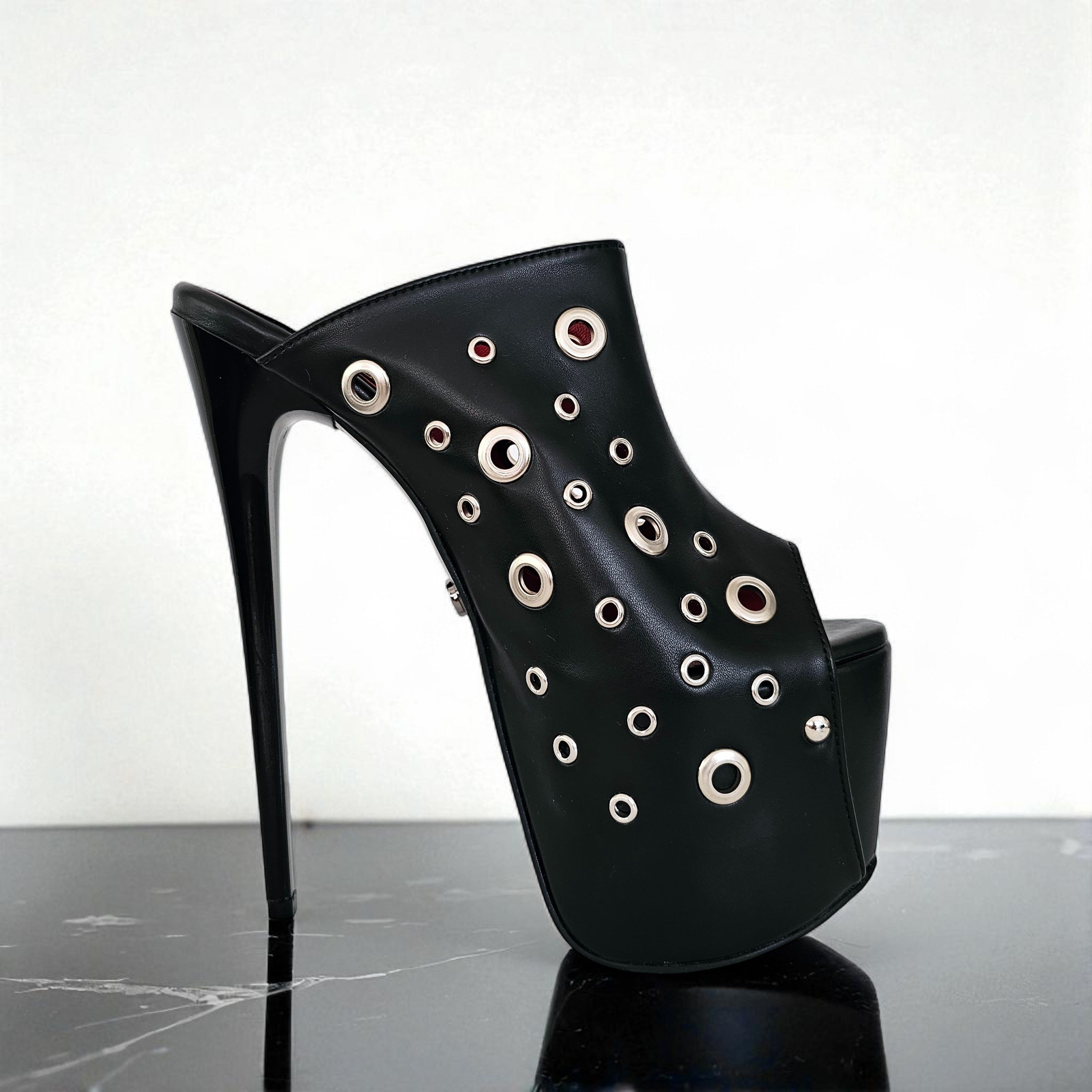Black high-heeled shoe with eyelet details on a reflective surface