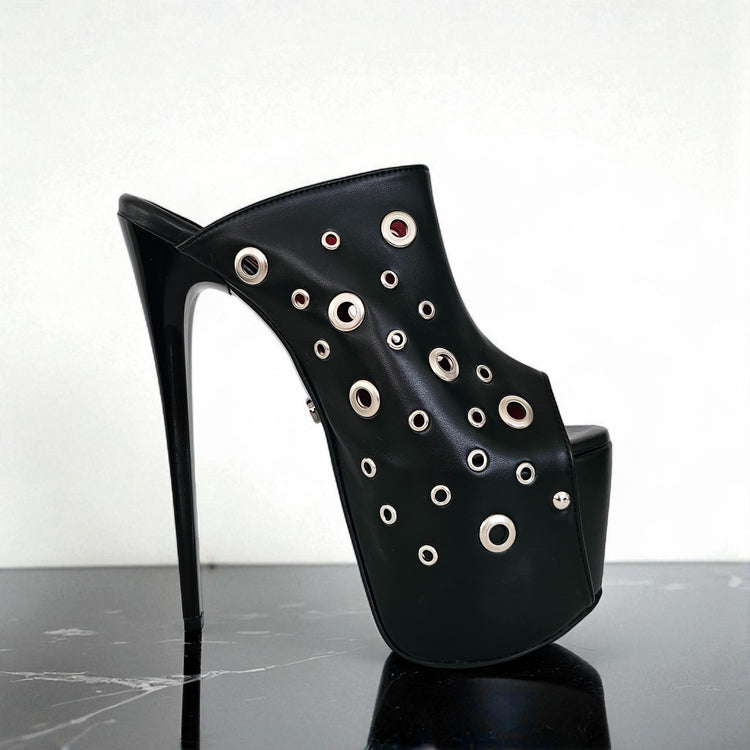 Black high-heeled shoe with eyelet details on a reflective surface
