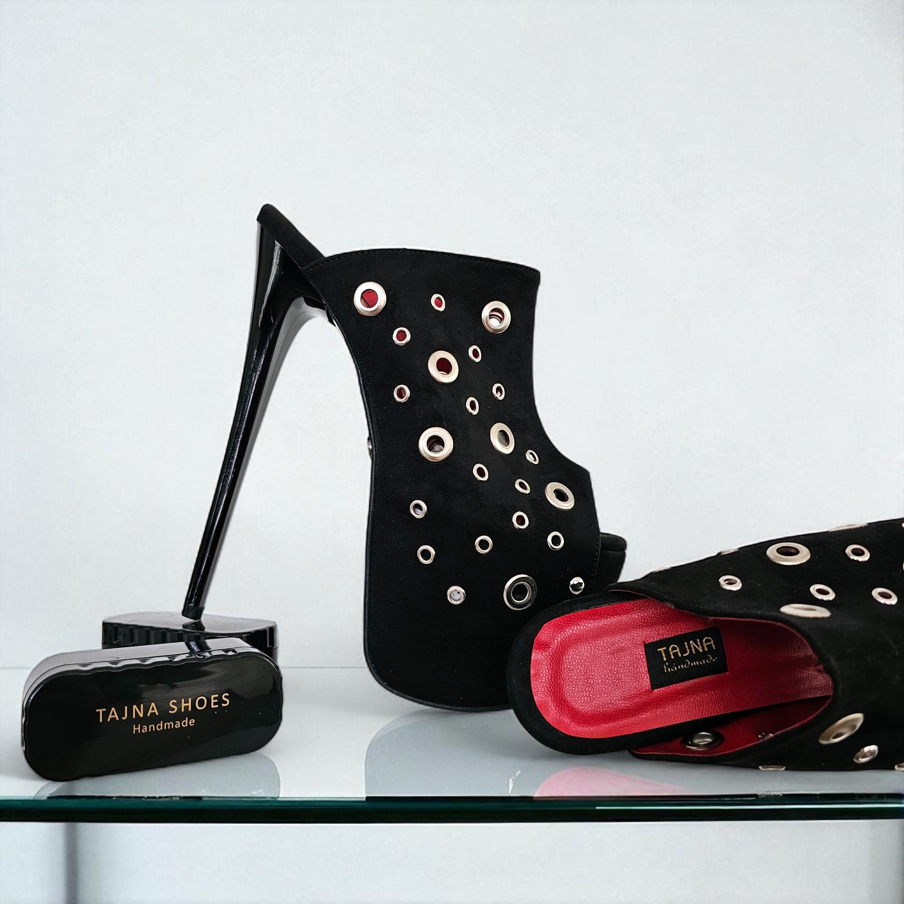 Black high-heeled shoes with eyelets and a Tajna branded box on a white background