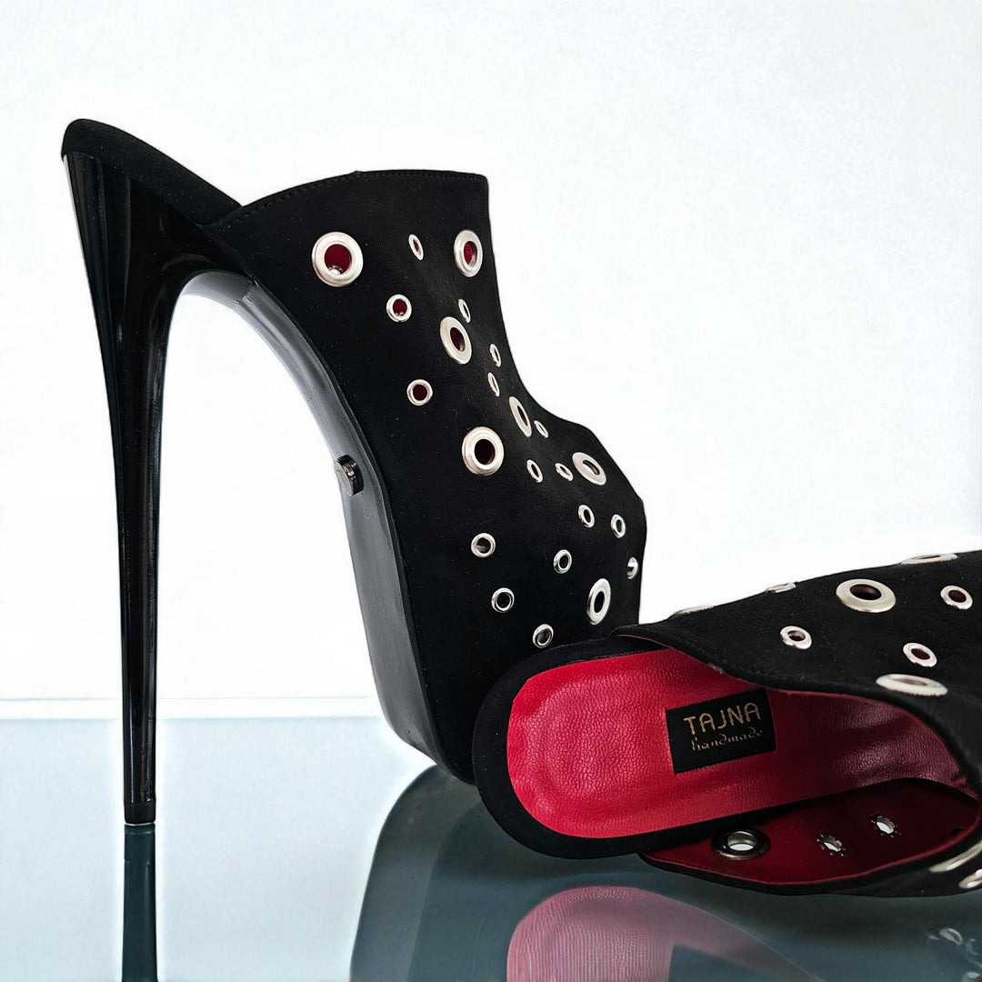 Black high-heeled shoe with eyelet design on a reflective surface