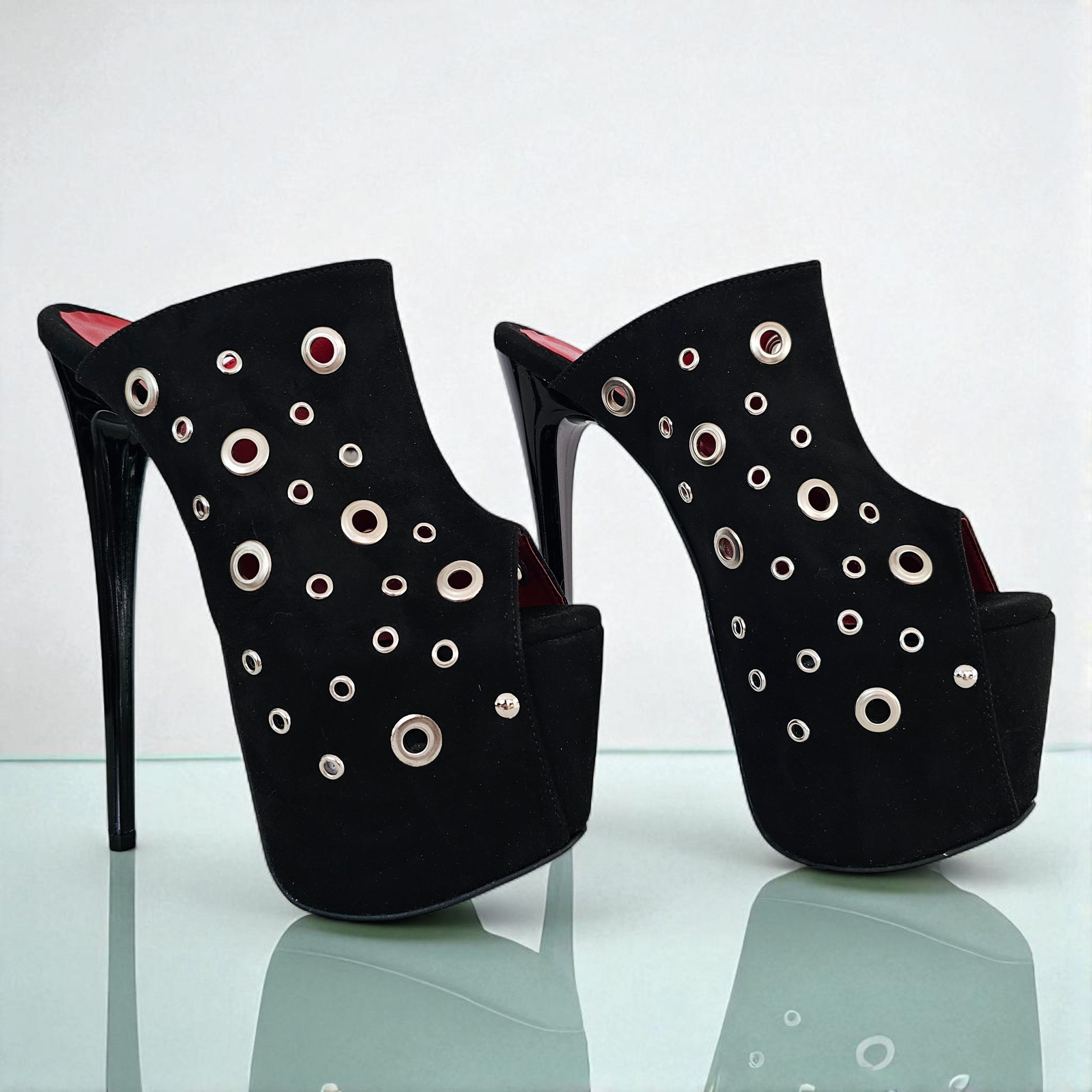 Black high-heeled shoes with circular embellishments on a reflective surface.