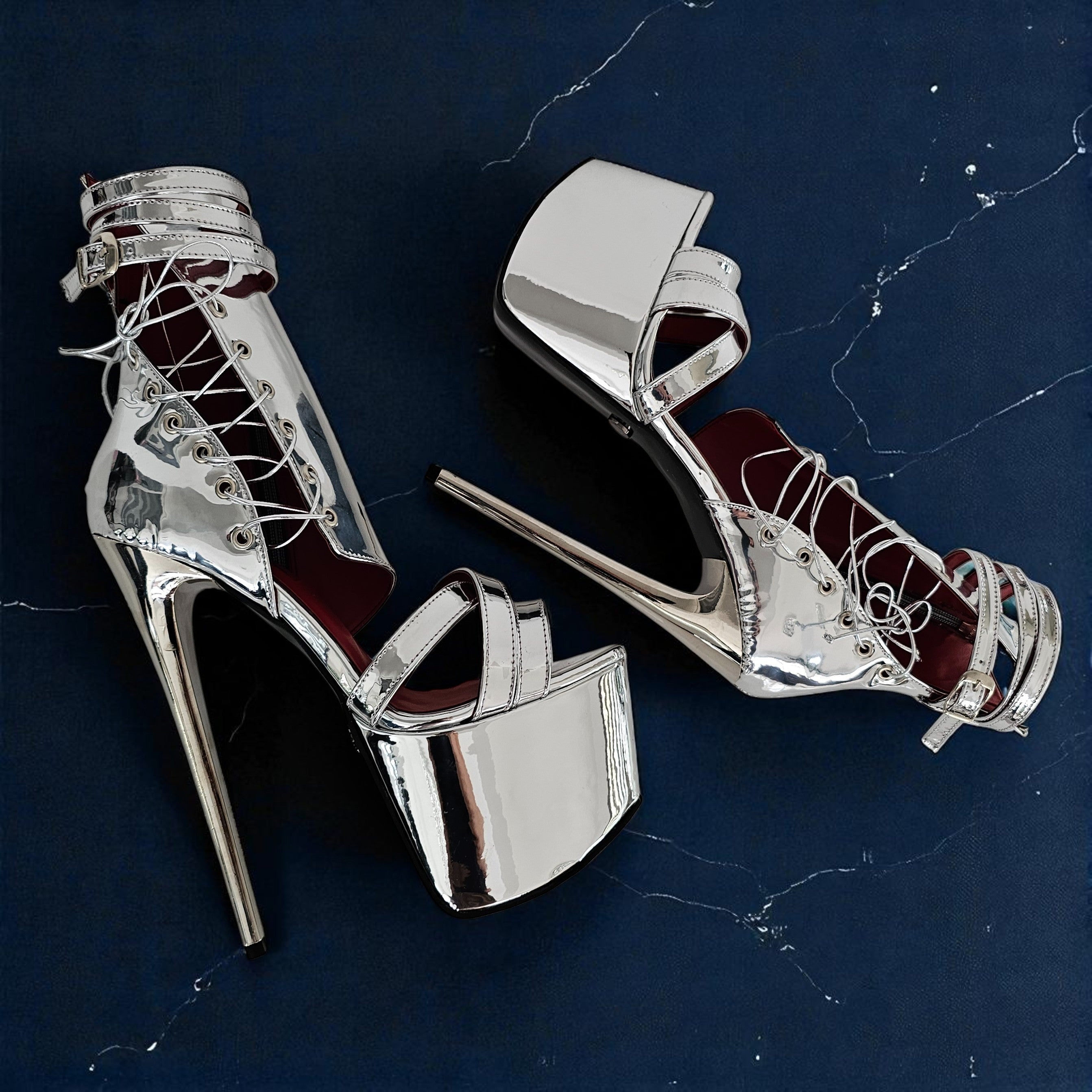 Silver high-heeled shoes with red interior on a dark blue marble surface