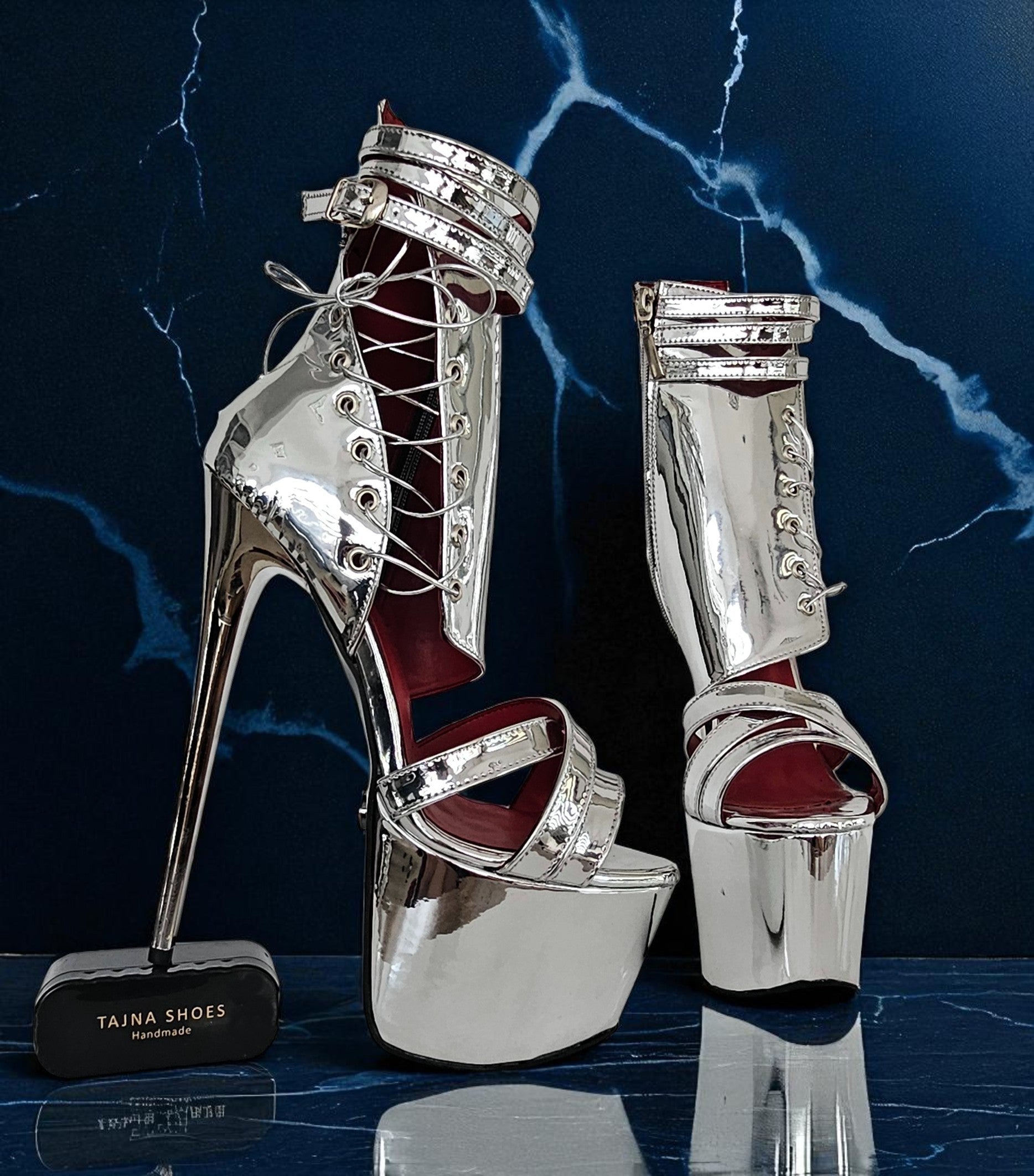 Silver high-heeled platform shoes with red soles on a dark blue marble background