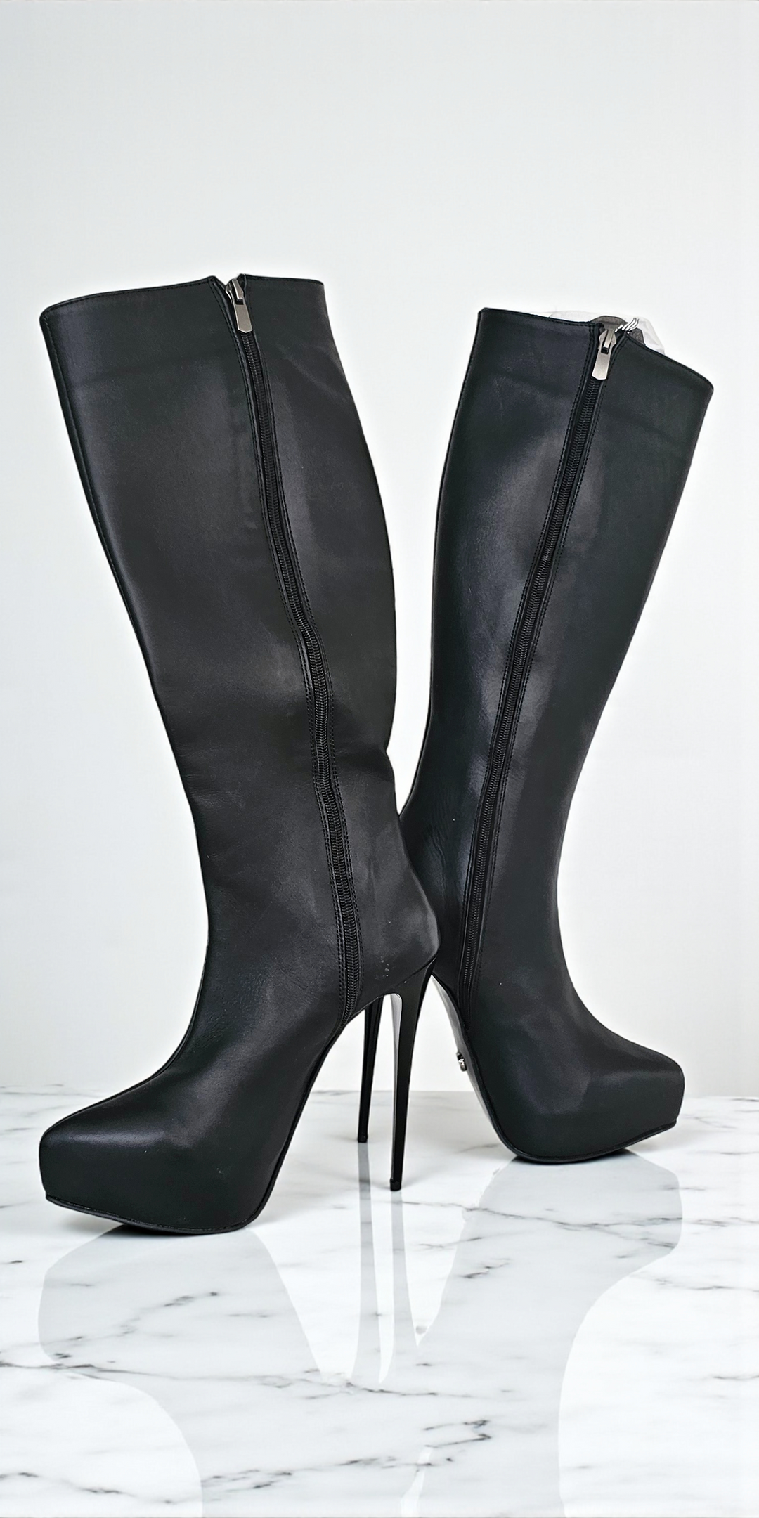 Black knee-high boots with high heels on a white marble surface