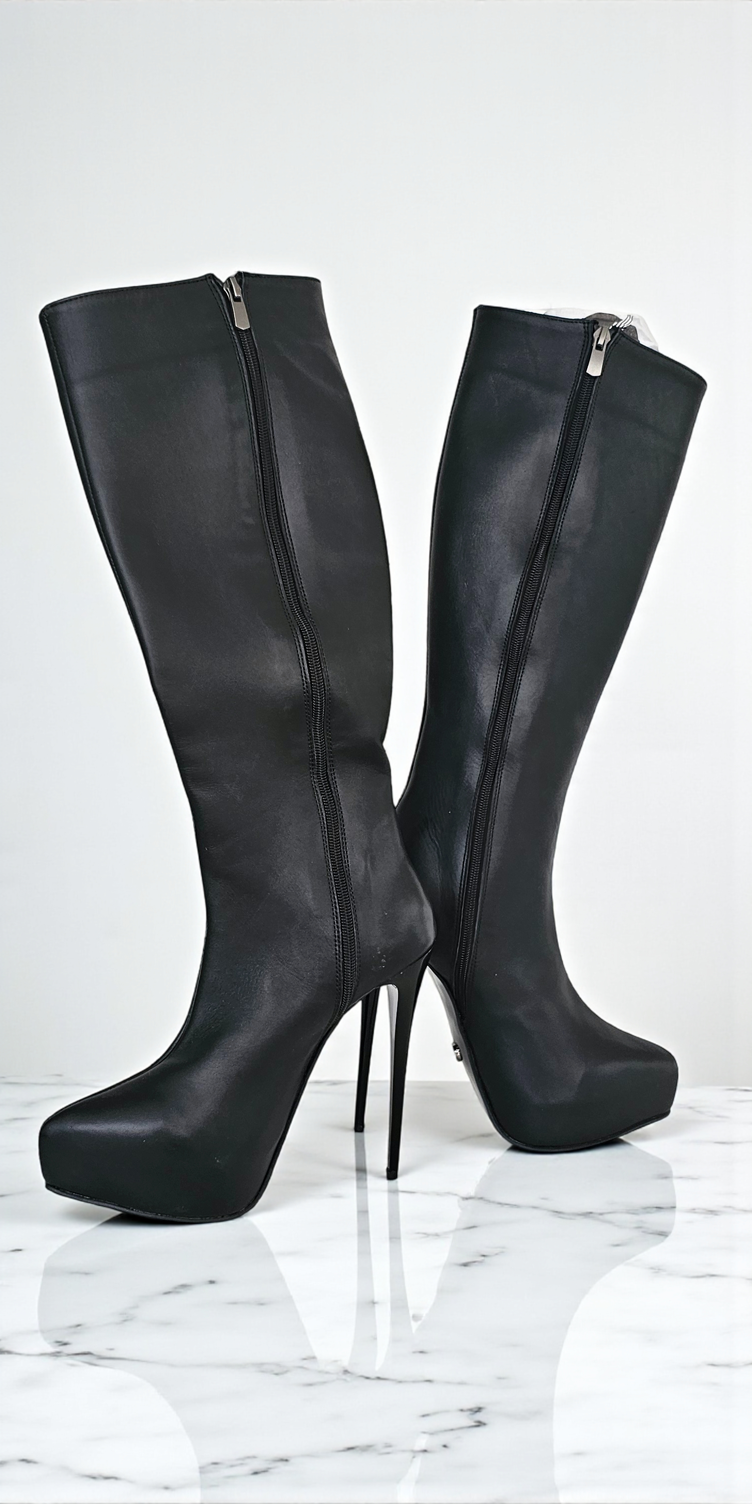 Black knee-high boots with high heels on a white marble surface