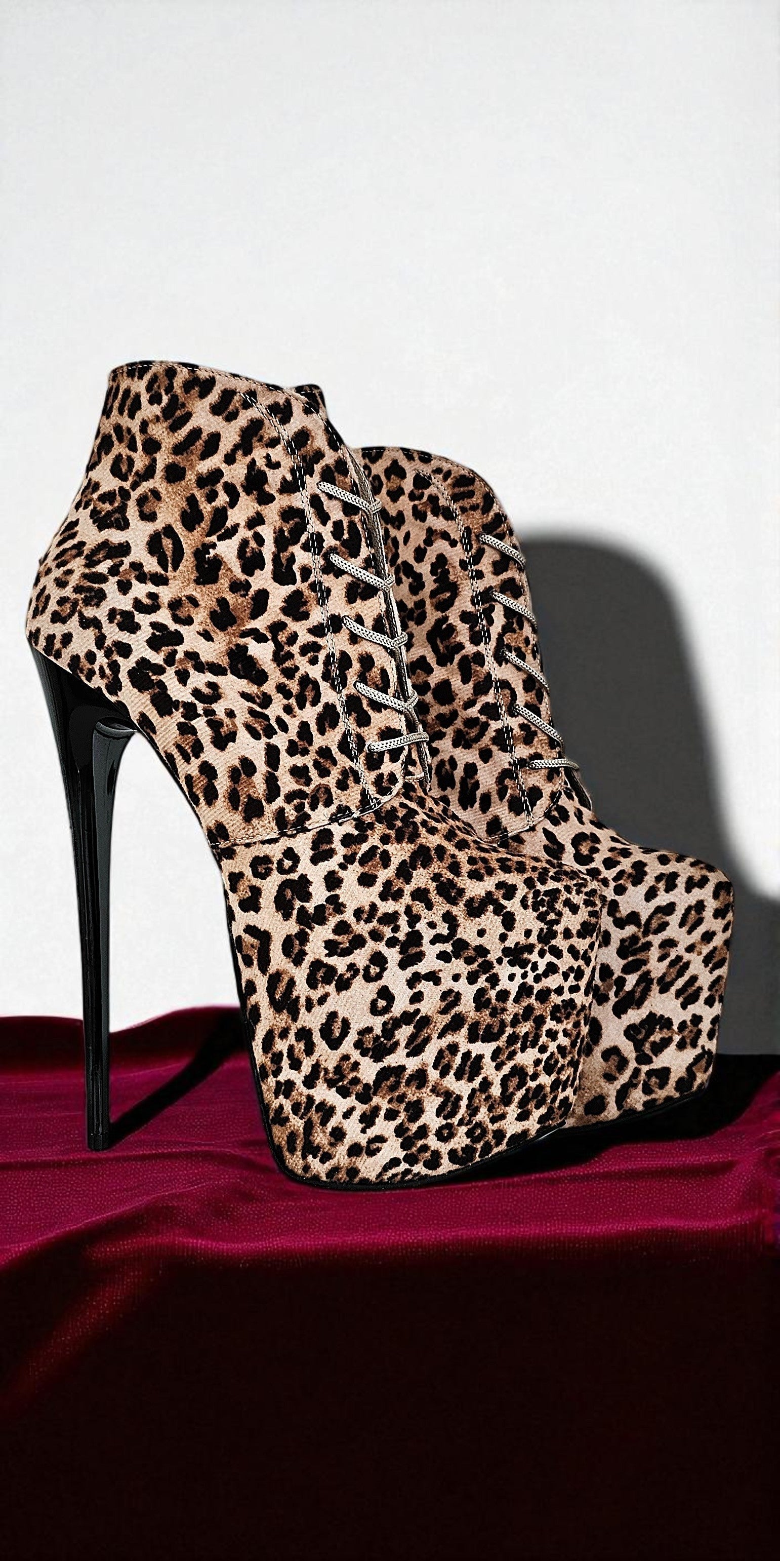Leopard print high-heeled platform boots on a red surface with a white background